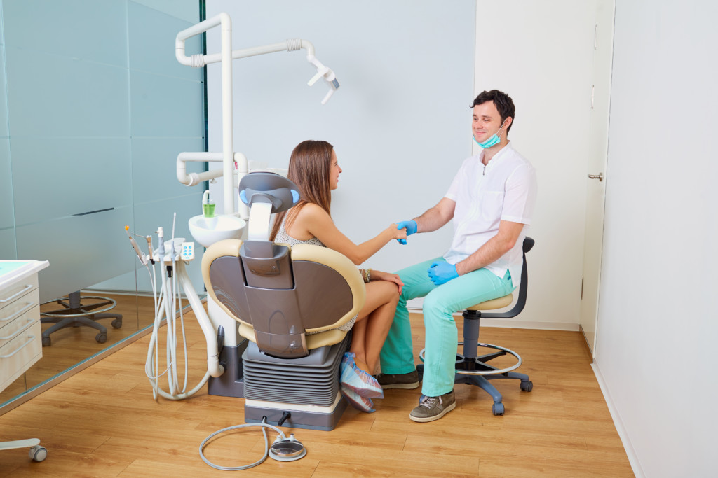 Dentist and patient, man and woman in doctor's office, shaking hands after patient care.