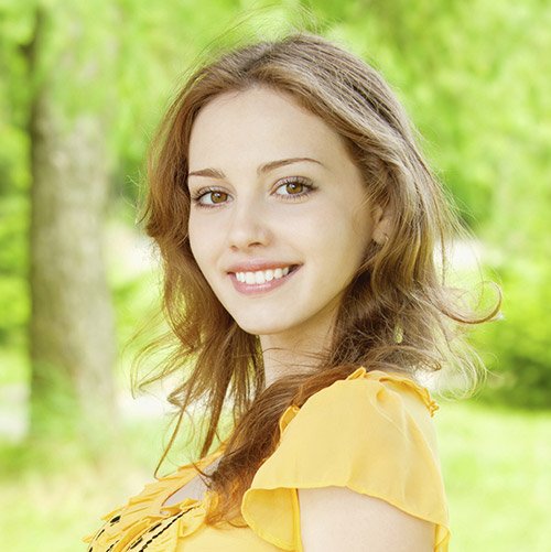 A young woman standing outside smiling to illustrate how cosmetic dentistry can transform your smile.
