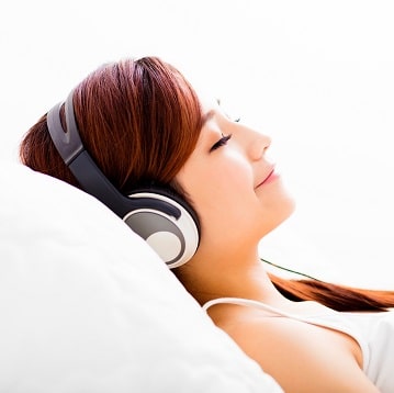 Relaxed woman laying back on pillow with headphones on.