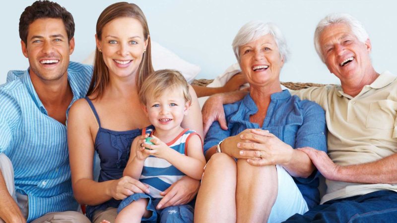 Happy multi-generational family including parents, a young child, and grandparents sitting together on a couch and smiling